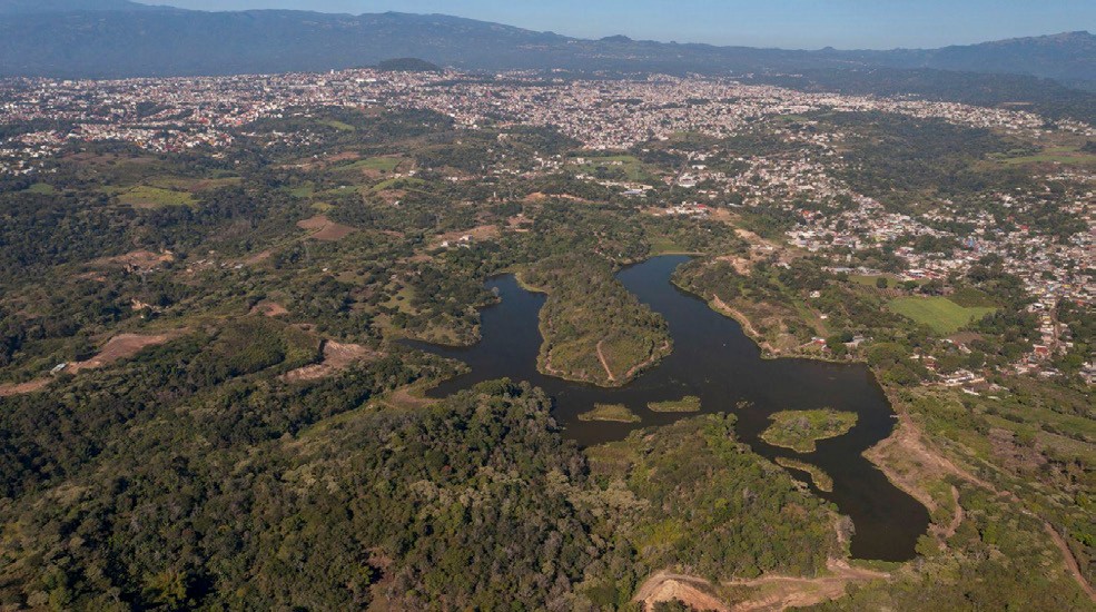 Vista aérea de la laguna del Castillo, tomada el 12 de diciembre de 2025. Se aprecian algunos de los tramos de la brecha alrededor del espejo de agua, más el aumento de otros caminos, construcciones y desmontes que han quedado con la tierra al descubierto (hacia abajo a la derecha). El crecimiento de la mancha urbana capitalina ha avanzado considerablemente al este (compárese arriba a la derecha de ambas fotografías). En las minas de arena que están en desuso, se reconoce cierta recuperación de la capa de vegetación. Fuente: Gerardo Sánchez Vigil.